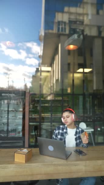 Kulaklıklı Güzel Bir Kız Öğle Yemeğini Yiyor Kafenin Penceresinin Arkasında — Stok video