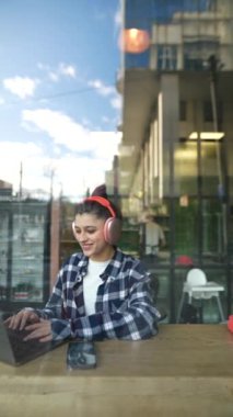 Kulaklıklı güzel bir kız kafenin penceresinin arkasında bilgisayarla vedalaşıyor. Yüksek kaliteli FullHD görüntüler