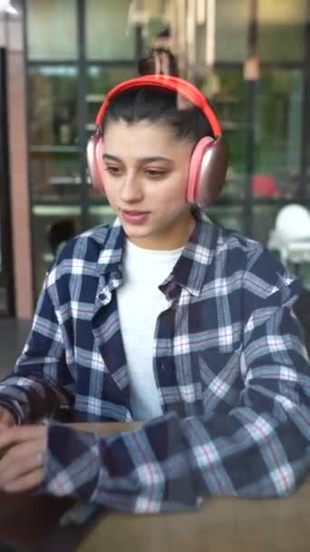 Gyönyörű Lány Fülhallgatóval Gépel Egy Okostelefonon Egy Laptoppal Ablak Mögött — Stock videók