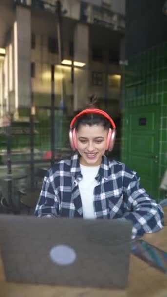 Gyönyörű Lány Fülhallgatóban Beszél Gépel Egy Laptopon Kávézóban Kiváló Minőségű — Stock videók