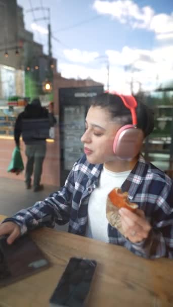 戴着耳机的漂亮姑娘在咖啡馆里用笔记本电脑吃午饭 听音乐 优质Fullhd影片 — 图库视频影像