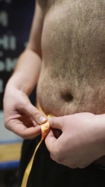 Sporcu adam spor salonunda belini bir santimetre bantla ölçüyor. Yüksek kaliteli FullHD görüntüler