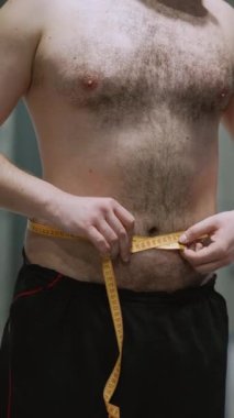 Sporcu adam spor salonunda belini bir santimetre bantla ölçüyor. Yüksek kaliteli FullHD görüntüler
