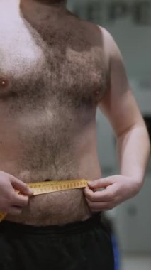 Sporcu adam spor salonunda belini bir santimetre bantla ölçüyor. Yüksek kaliteli FullHD görüntüler