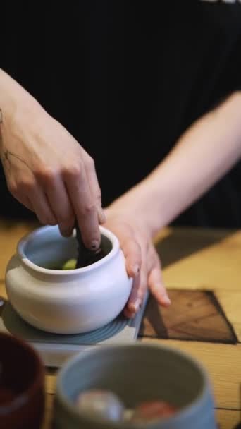 木製のテーブルの上に白いボウルに緑茶を作る抹茶プロセス 茶色いテーブルの上で抹茶を点てる 女性は抹茶有機緑茶粉末を木のスプーンでボウルに注ぐ — ストック動画