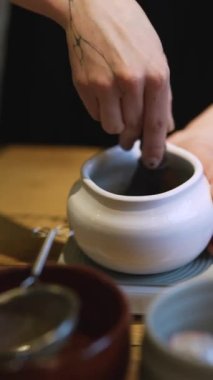 Ahşap masa arkasında beyaz kasede yeşil çay yapma süreci. Kahverengi masada fincanda kibrit yeşil çay. Kadın, ahşap kaşıkla kibrit kutusuna organik yeşil çay tozu döküyor.. 