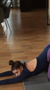 İki güzel kız evde yoga egzersizleri yapıyor. Vücutlarını esneterek alıştırma yapıyorlar. Gençler, iç mekanlar ve sağlıklı yaşam tarzı konsepti.
