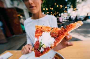 Kadın eli terasta bir dilim pizzayı tutuyor.. 