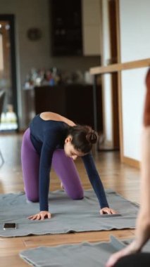 İki güzel kız evde yoga egzersizleri yapıyor. Vücutlarını esneterek alıştırma yapıyorlar. Gençler, iç mekanlar ve sağlıklı yaşam tarzı konsepti.