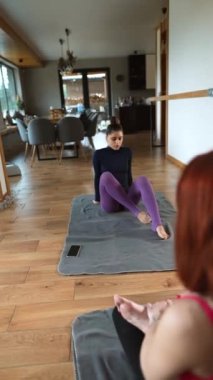 İki güzel kız evde yoga egzersizleri yapıyor. Vücutlarını esneterek alıştırma yapıyorlar. Gençler, iç mekanlar ve sağlıklı yaşam tarzı konsepti.