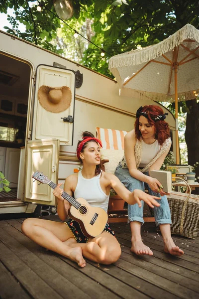 幸せなヒッピーの女の子は キャンパートレーラーでギターを弾くのに楽しい時間を過ごしています 旅行のコンセプト 高品質の写真 — ストック写真