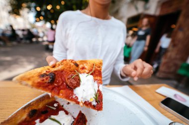 Kadın eli terasta bir dilim pizzayı tutuyor.. 
