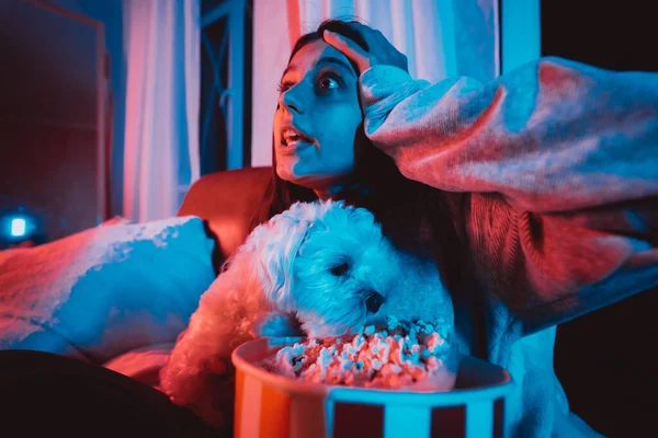 漂亮的小女孩在家里黑暗的房间里 拿着爆米花桶和她的狗玩耍 坐在监视器或电视前看电影 疯狂的感情高质量的照片 — 图库照片