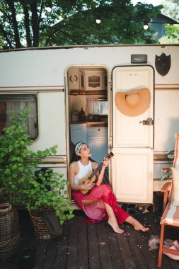 Mutlu hippi kız karavanda gitar çalarak iyi vakit geçiriyor. Tatil, tatil, gezi konsepti. Yüksek kalite fotoğraf.