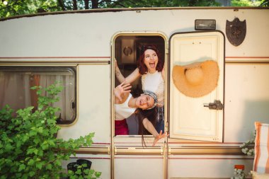 Happy hippie friends are having a good time together in a camper trailer. Holiday, vacation, trip concept. High quality photo clipart