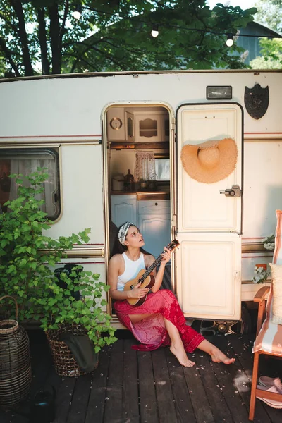 ハッピーヒッピーの女の子は キャンパートレーラーでギターを弾くのに楽しい時間を過ごしています 旅行のコンセプト 高品質の写真 — ストック写真