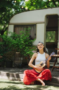 Mutlu hippi kız karavanda gitar çalarak iyi vakit geçiriyor. Tatil, tatil, gezi konsepti. Yüksek kalite fotoğraf.