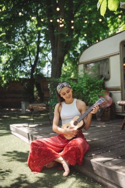 Mutlu hippi kız karavanda gitar çalarak iyi vakit geçiriyor. Tatil, tatil, gezi konsepti. Yüksek kalite fotoğraf.