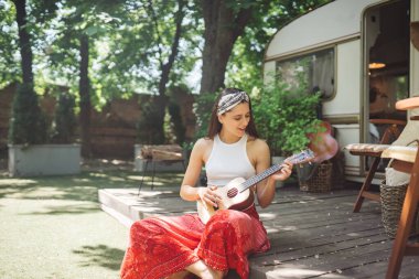 Mutlu hippi kız karavanda gitar çalarak iyi vakit geçiriyor. Tatil, tatil, gezi konsepti. Yüksek kalite fotoğraf.