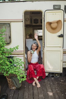 Happy hippie girl are having a good time with cup of tea in camper trailer. Holiday, vacation, trip concept.High quality photo clipart
