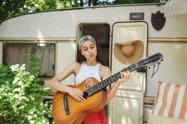 Mutlu hippi kız karavanda gitar çalarak iyi vakit geçiriyor. Tatil, tatil, gezi konsepti. Yüksek kalite fotoğraf.