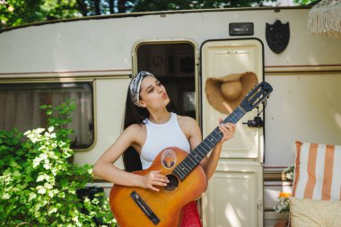 Mutlu hippi kız karavanda gitar çalarak iyi vakit geçiriyor. Tatil, tatil, gezi konsepti. Yüksek kalite fotoğraf.