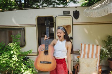 Mutlu hippi kız karavanda gitar çalarak iyi vakit geçiriyor. Tatil, tatil, gezi konsepti. Yüksek kalite fotoğraf.