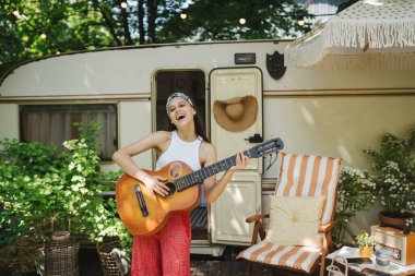 Mutlu hippi kız karavanda gitar çalarak iyi vakit geçiriyor. Tatil, tatil, gezi konsepti. Yüksek kalite fotoğraf.