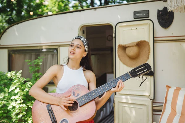 stock image Happy hippie girl are having a good time with playing on guitar in camper trailer. Holiday, vacation, trip concept.High quality photo