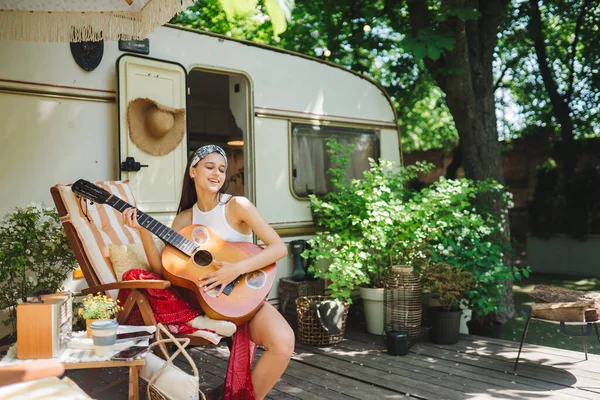 Mutlu hippi kız karavanda gitar çalarak iyi vakit geçiriyor. Tatil, tatil, gezi konsepti. Yüksek kalite fotoğraf.