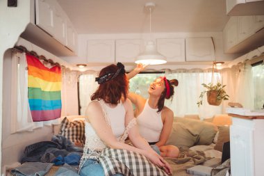 Sevimli lezbiyen bir çiftin portresi. İki kız, duvarında LGBT bayrağı olan bir karavanda şefkatle vakit geçiriyorlar. Aşk ve tutum. LGBT konsepti. Yüksek kalite fotoğraf