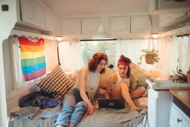 Sevimli lezbiyen bir çiftin portresi. İki kız, karavanda dizüstü bilgisayarda, duvarında LGBT bayrağı olan bir film izleyerek nazikçe zaman geçiriyorlar. Aşk ve tutum. LGBT konsepti. Yüksek kalite fotoğraf