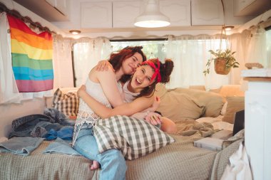 Sevimli lezbiyen bir çiftin portresi. İki kız, duvarında LGBT bayrağı olan bir karavanda şefkatle vakit geçiriyorlar. Aşk ve tutum. LGBT konsepti. Yüksek kalite fotoğraf