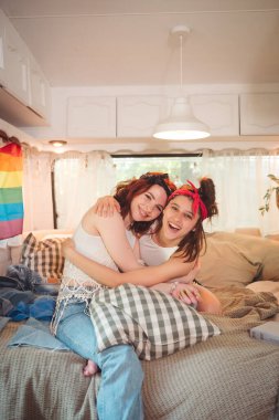 Sevimli lezbiyen bir çiftin portresi. İki kız, duvarında LGBT bayrağı olan bir karavanda şefkatle vakit geçiriyorlar. Aşk ve tutum. LGBT konsepti. Yüksek kalite fotoğraf