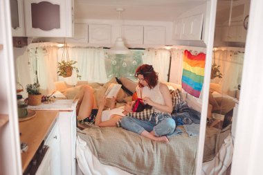 Sevimli lezbiyen bir çiftin portresi. İki kız, duvarında LGBT bayrağı olan bir karavanda şefkatle vakit geçiriyorlar. Aşk ve tutum. LGBT konsepti. Yüksek kalite fotoğraf