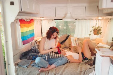 Sevimli lezbiyen bir çiftin portresi. İki kız, duvarında LGBT bayrağı olan bir karavanda şefkatle vakit geçiriyorlar. Aşk ve tutum. LGBT konsepti. Yüksek kalite fotoğraf