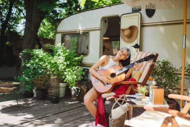 Mutlu hippi kız karavanda gitar çalarak iyi vakit geçiriyor. Tatil, tatil, gezi konsepti. Yüksek kalite fotoğraf.
