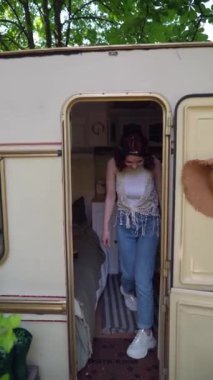 The beautiful hippie girl steps out of the trailer and looks around . High quality 4k footage