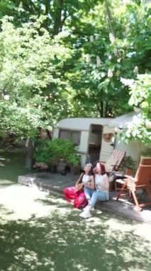 camera zooms in Two beautiful hippie girls are singing a song sitting on the terrace near the trailer with a guitar. High quality 4k footage