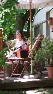  beautiful hippie girl is singing a song and playing the guitar near the trailer. High quality 4k footage