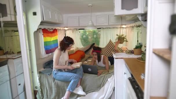 Two Beautiful Hippie Girls Sitting Bed Trailer Chatting Laptop Book — Stockvideo