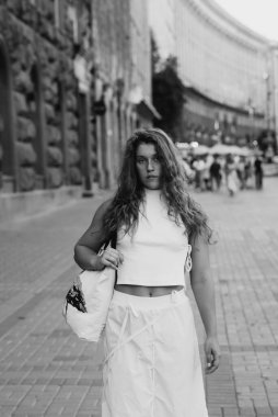 A trendy girl in a white outfit and curly hair on the city streets. High quality photo