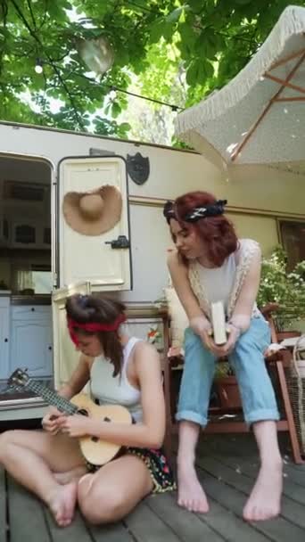 两个嬉皮士女孩在拖车边 一个在弹吉他 另一个手里拿着一本书 高质量的4K镜头 — 图库视频影像