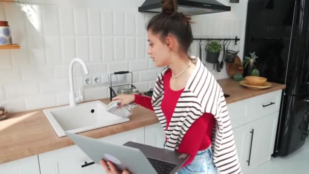 Mladá Krásná Dívka Vesele Povídá Svým Laptopem Zatímco Uklízí Kuchyni — Stock video