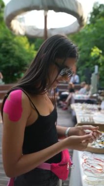 Bileklerinde pembe bantlarla hayat dolu genç bir kadın fuarda mücevher seçiyor. Yüksek kaliteli FullHD görüntüler