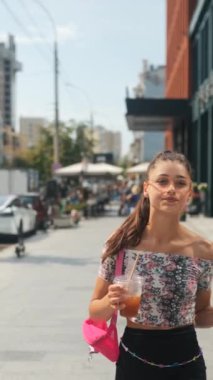 Şehir sokaklarında elinde soğuk bir kahve ve akıllı bir telefonla şık, hayat dolu genç bir kadın. Yüksek kalite 4k görüntü