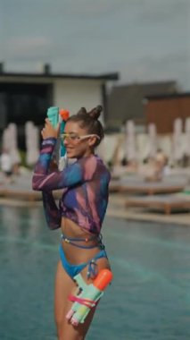 Çarpıcı genç bir kadın havuz kenarında su tabancalarıyla dans ediyor. Yüksek kalite 4k görüntü