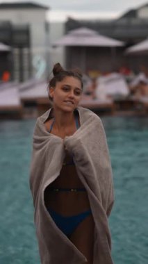Yağmurda zarif bir şekilde dans eden havluyla ve mayosuyla renkli genç bir bayan havuza neşe katıyor. Yüksek kalite 4k görüntü