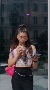 Elinde canlandırıcı bir içecek olan genç ve güzel bir kız akıllı telefonuyla mesajlaşıyor. Yüksek kalite 4k görüntü