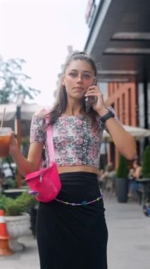 Elinde ferahlatıcı bir içecekle çekici genç bir kadın sokakta telefonla konuşuyor. Yüksek kalite 4k görüntü
